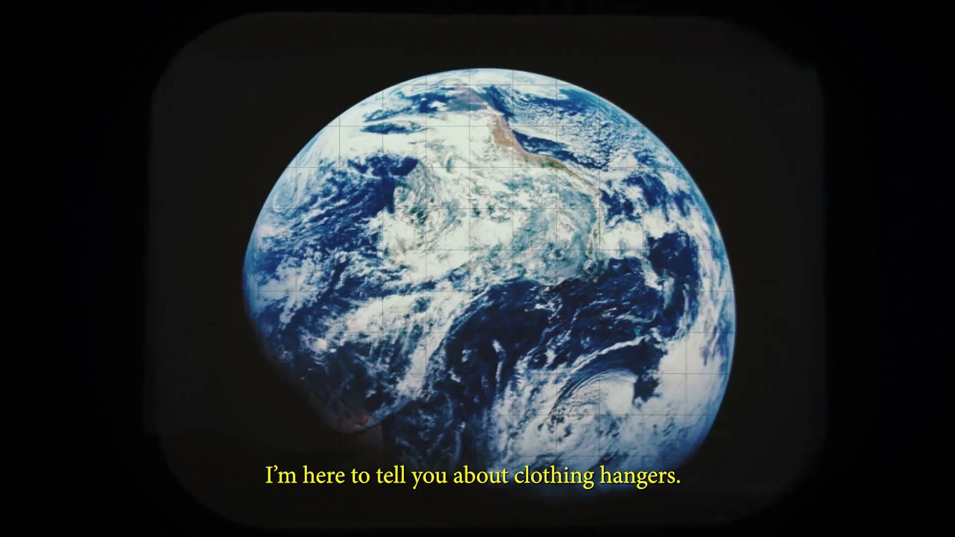 A shot of planet Earth from space, with a grid overlay, displayed on an old television screen, with yellow subtitles at the bottom.