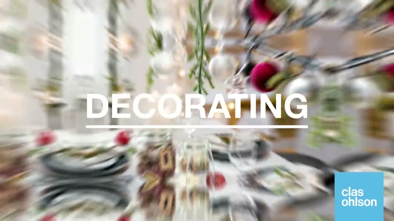 A festive Christmas table is set with plates, glasses, and jars of food, adorned with hanging ornaments and pine branches, with the word "DECORATING" superimposed.