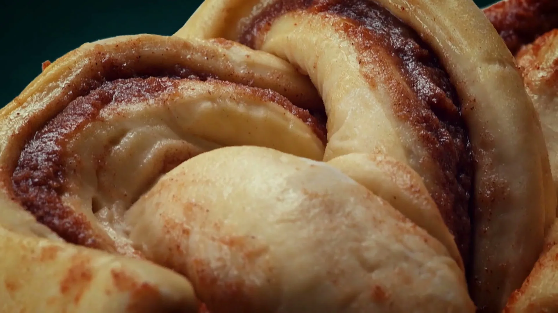 A close-up shot of a freshly baked cinnamon roll, showing its intricate swirls of dough and cinnamon sugar, against a dark background.