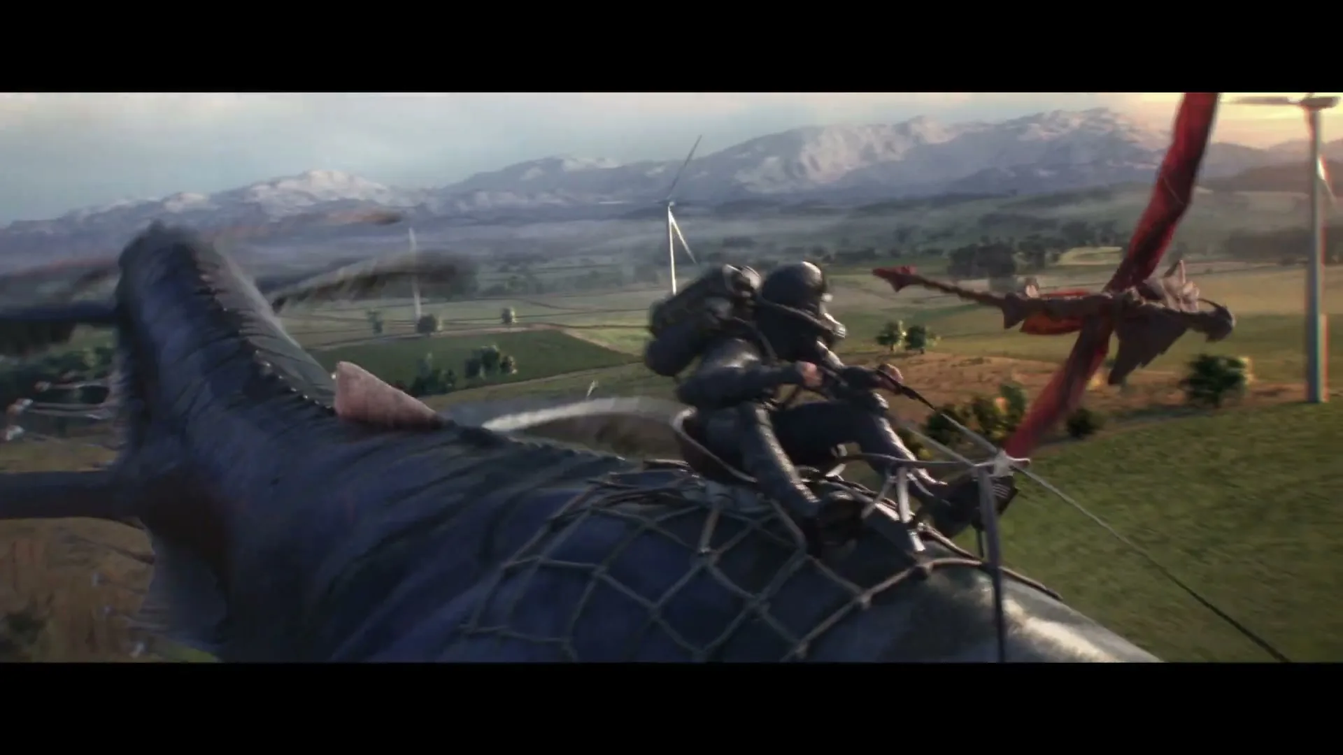 A person in dark gear rides a large, dark blue flying creature, with a smaller red creature flying nearby, over a green landscape with wind turbines and mountains.