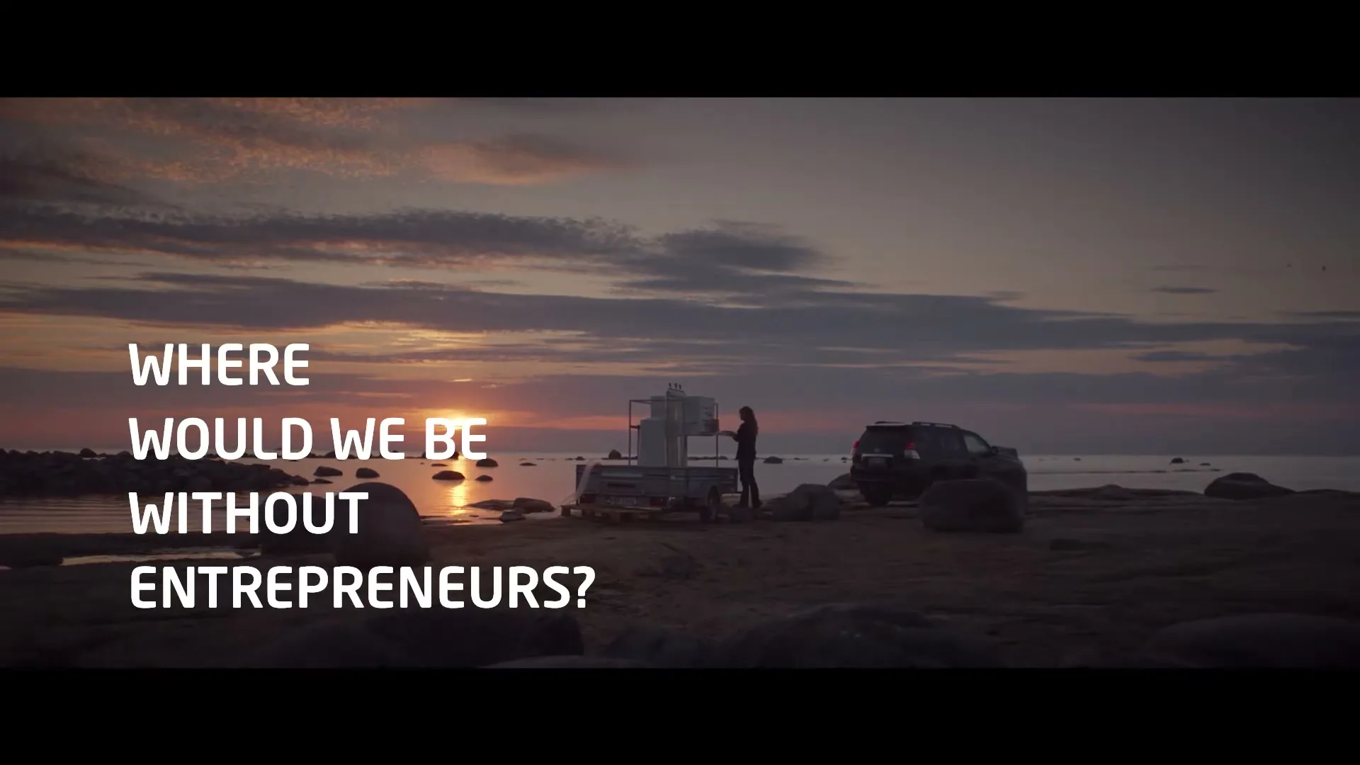 A person stands next to a small boat on a rocky beach at sunset, with a car parked nearby and text overlayed on the screen.