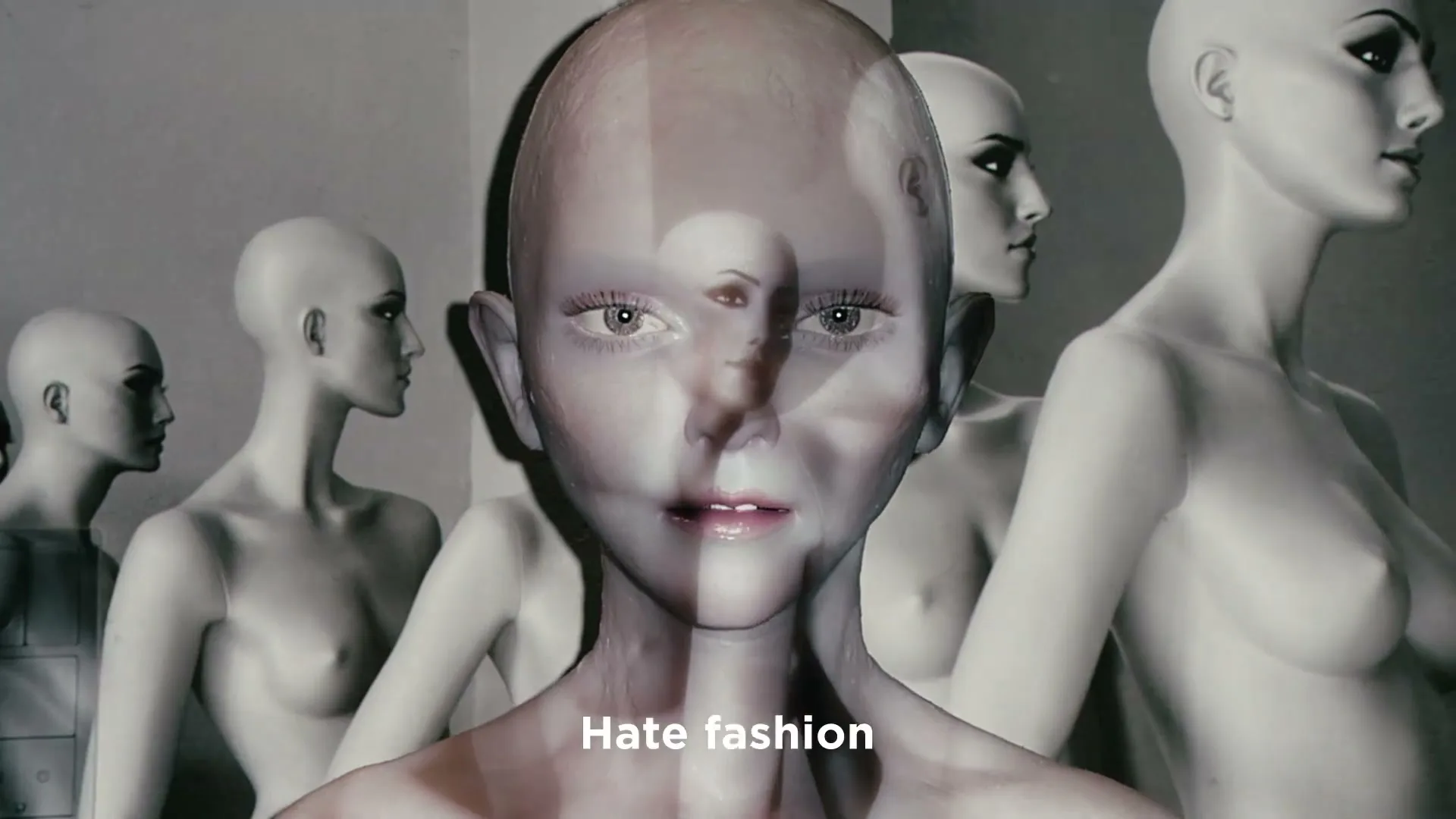 A translucent, bald, androgynous figure with human eyes and mouth is superimposed over a line of bald mannequins in a studio.