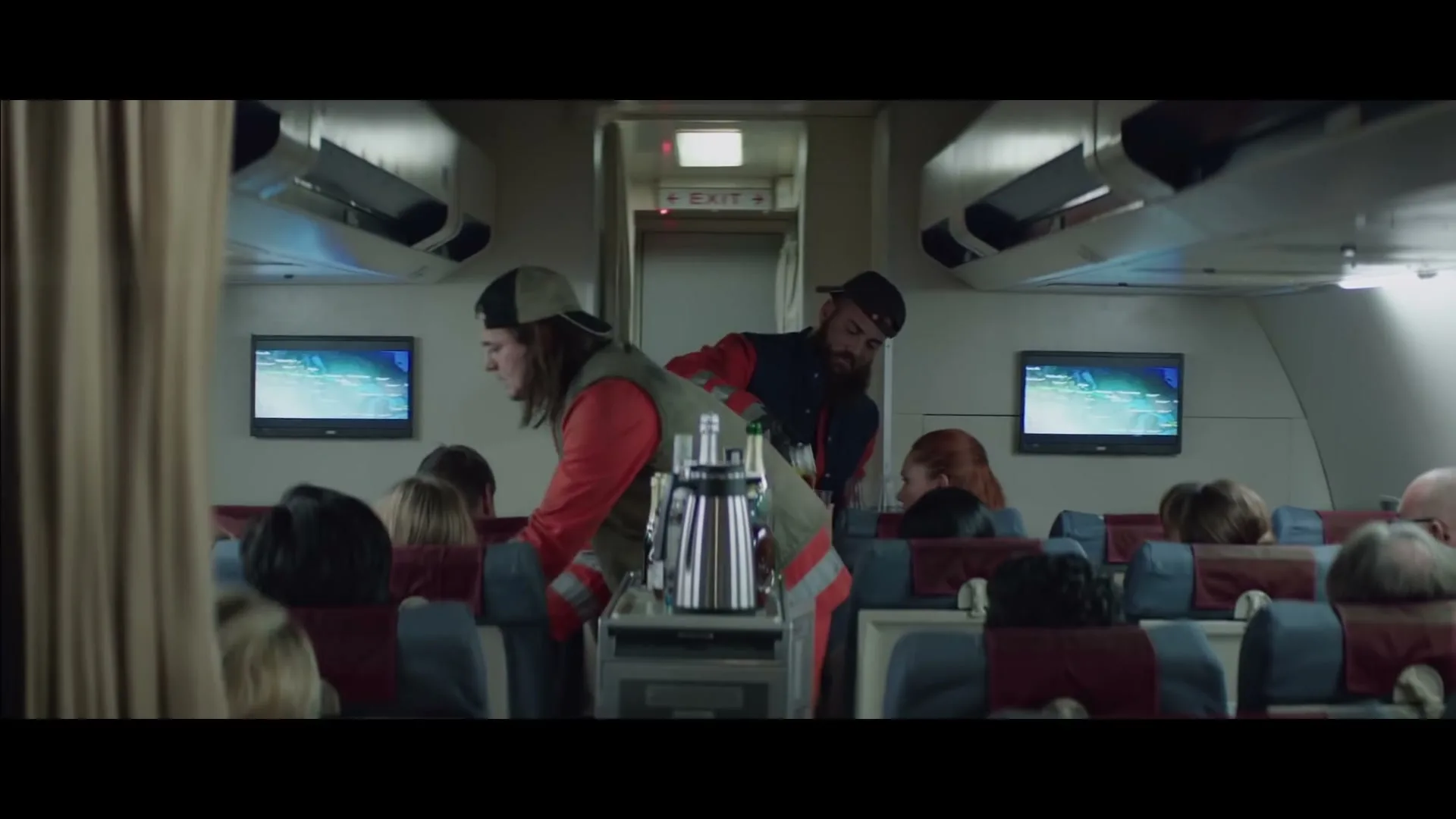 Two male garbage collectors, dressed in work uniforms and caps, serve drinks from a trolley to passengers on an airplane.
