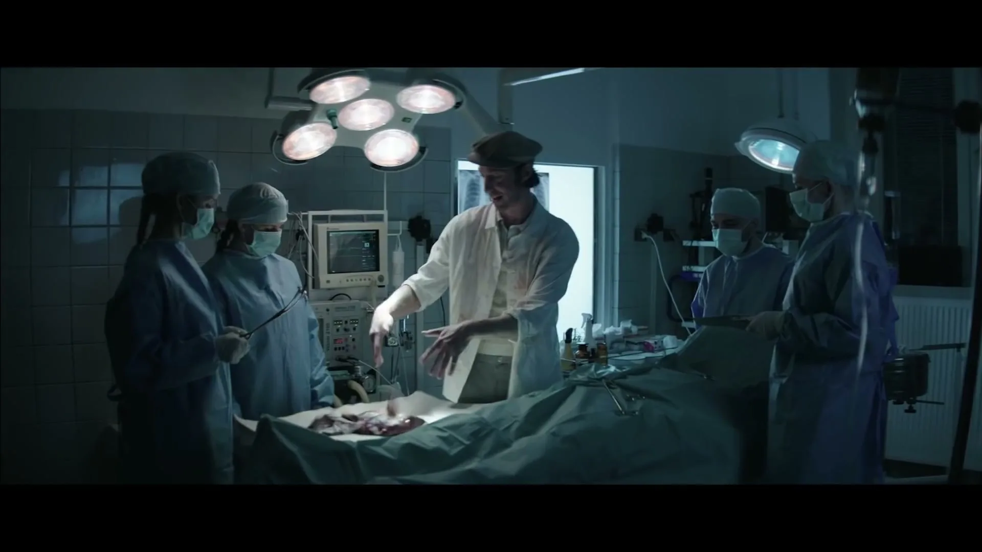A man in a butcher's hat and white coat, surrounded by surgeons, places a piece of meat on an operating table in a hospital operating room.