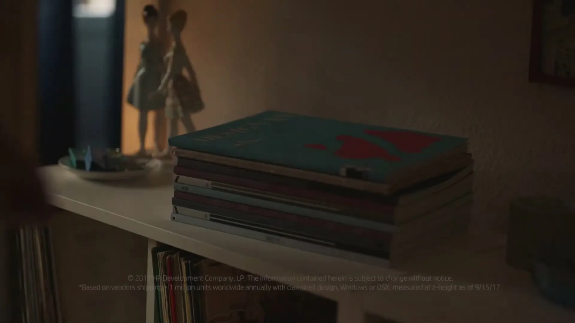 A person's hands place a thin, light-colored object on a stack of magazines on a white shelf in a dimly lit room.