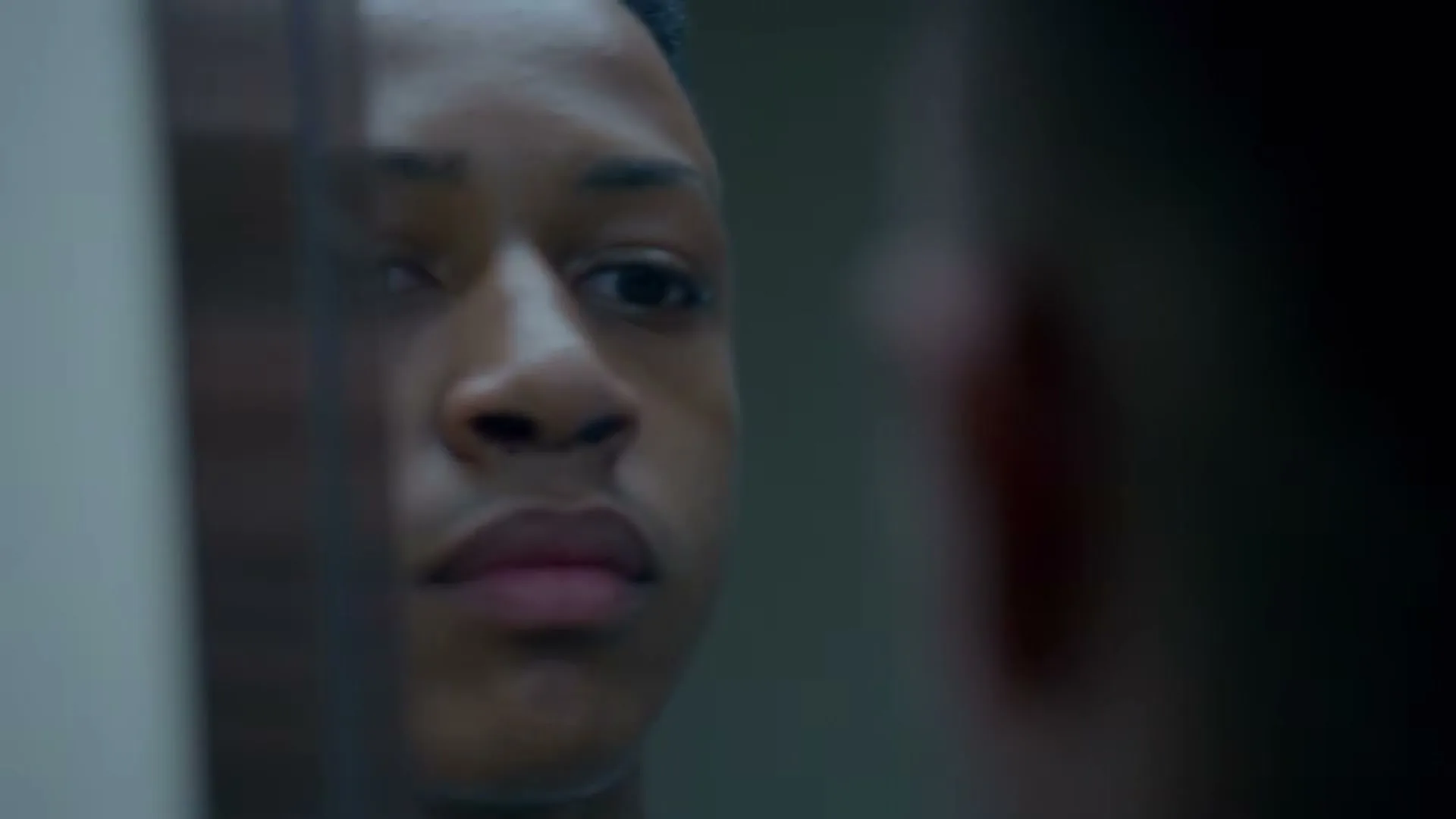 A young male patient with a nose ring looks at his reflection in a mirror in a hospital room.