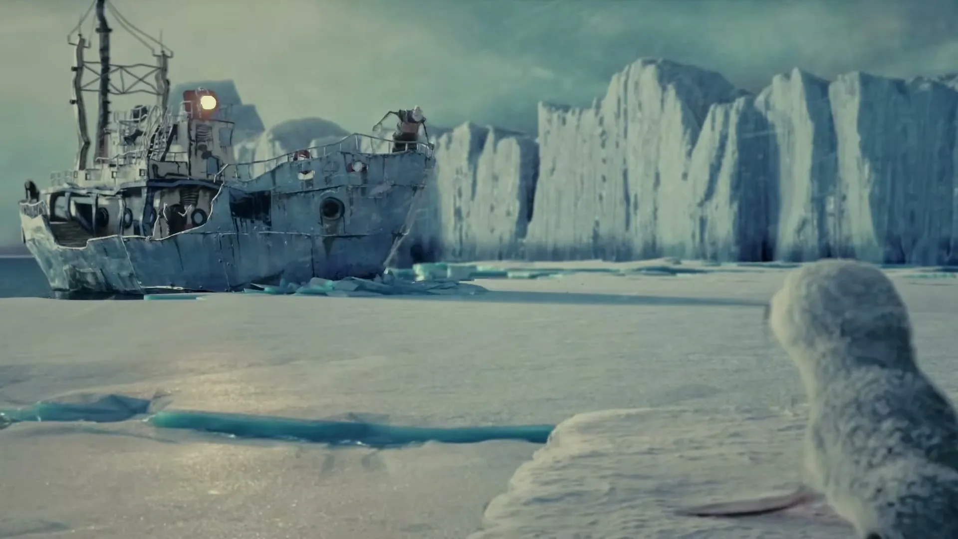 Two baby seals look at a large, old ship stuck in the ice, with icebergs in the background under a cloudy sky.