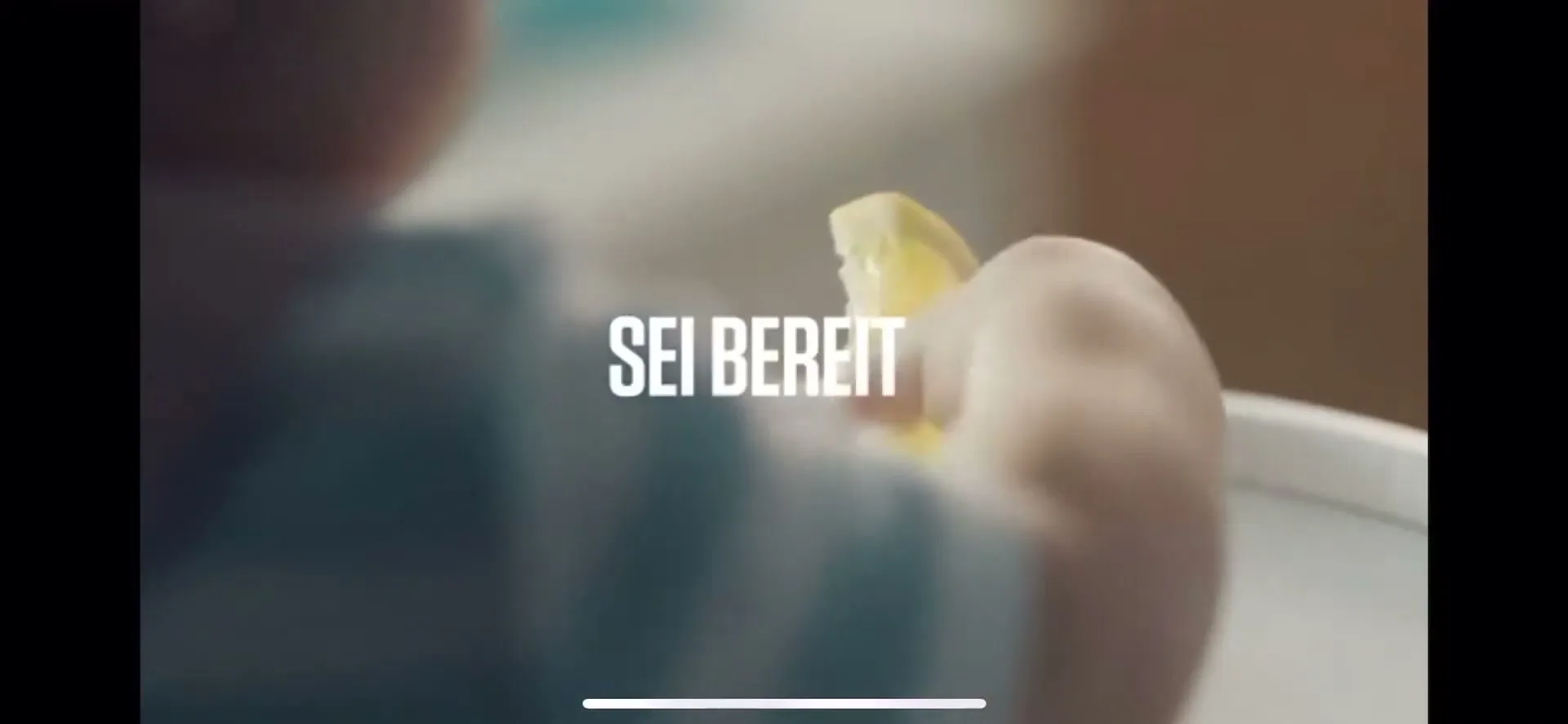 A baby in a high chair holds a lemon slice, with the text "SEI BEREIT_" overlaid on the image.