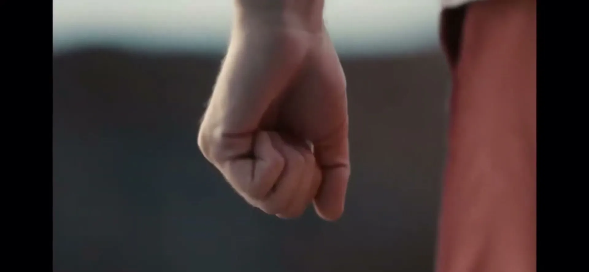 A person's hand clenches into a fist, showing determination or tension, against a blurred background.