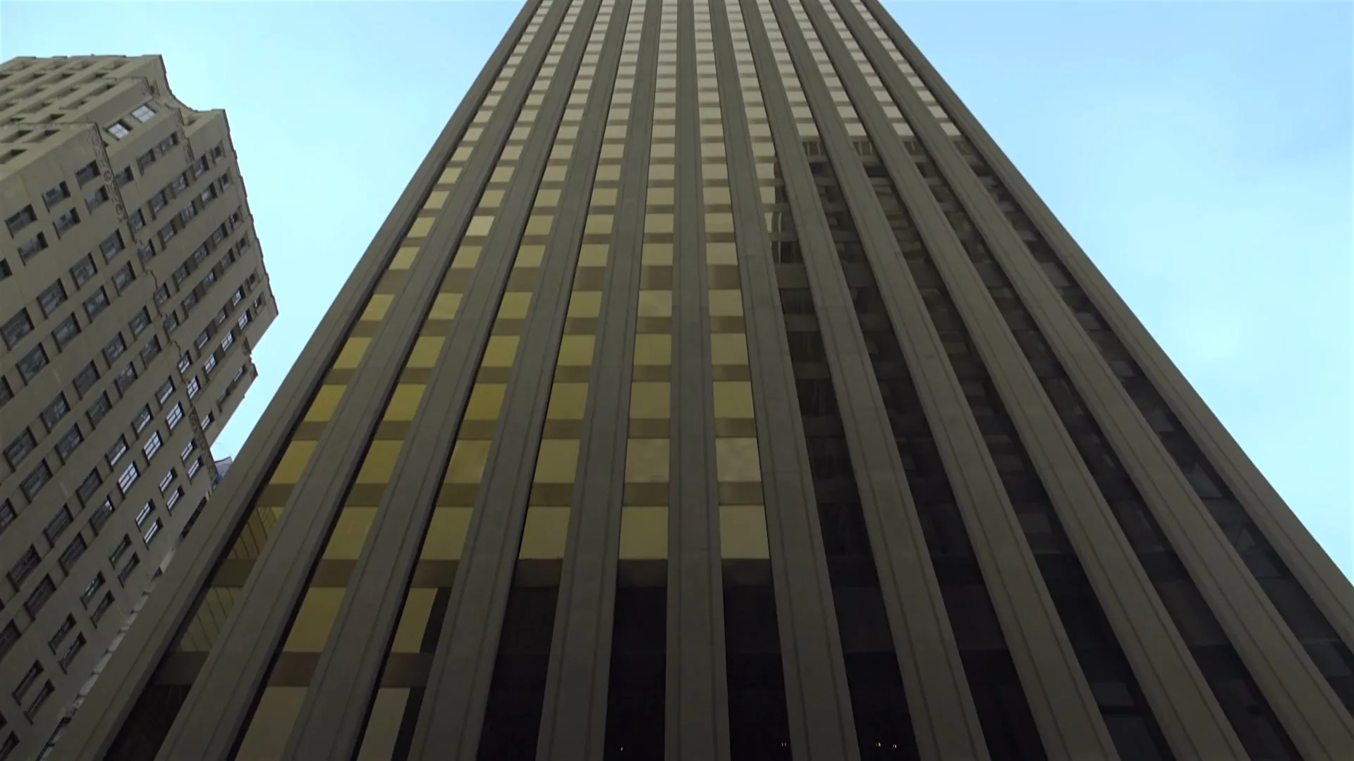 A low-angle shot of a tall, modern skyscraper with many windows, against a clear blue sky, suggesting a corporate setting.
