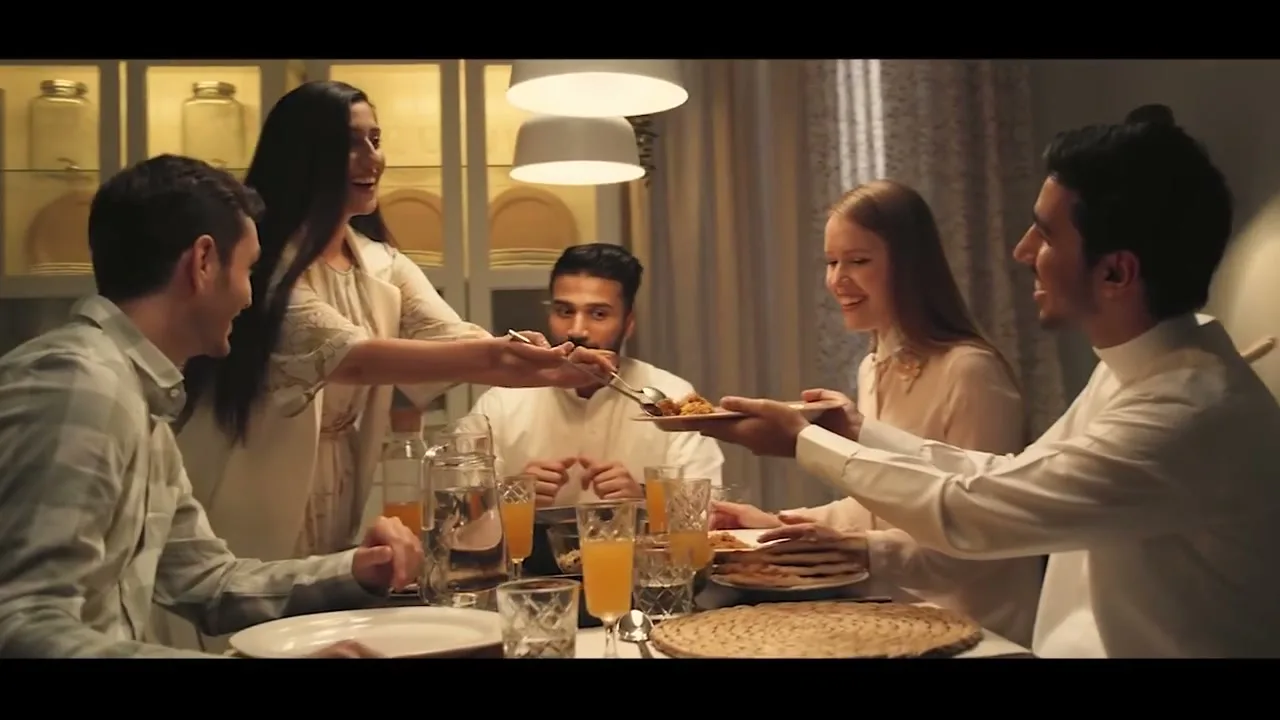 A diverse group of friends shares food around a dining table in a warm, inviting home, laughing and enjoying each other's company.