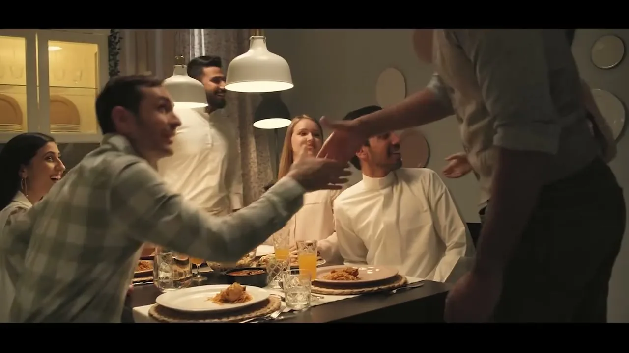 A diverse group of friends gathers around a dining table, sharing a meal and shaking hands, in a warm, inviting home setting.