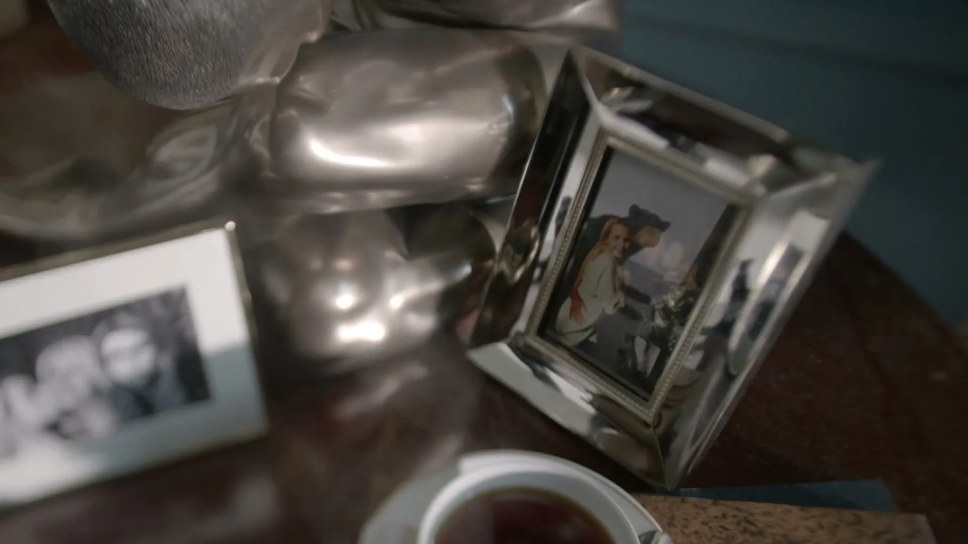 A close-up shot of a silver framed photo of a woman and two children on a wooden table, next to a cup of tea.