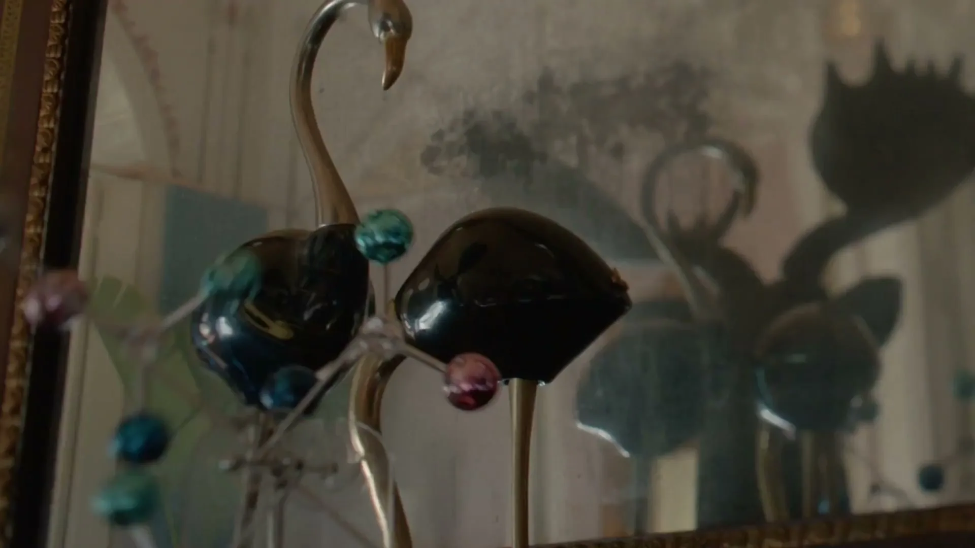 A close-up shot of a decorative swan figurine with colorful spheres, reflected in an antique mirror, in a dimly lit room.
