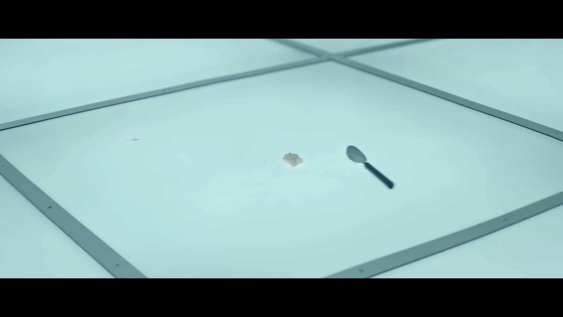 A small metal spoon with a black handle is thrown onto a white, sterile-looking surface, landing next to a small blob of ice cream.