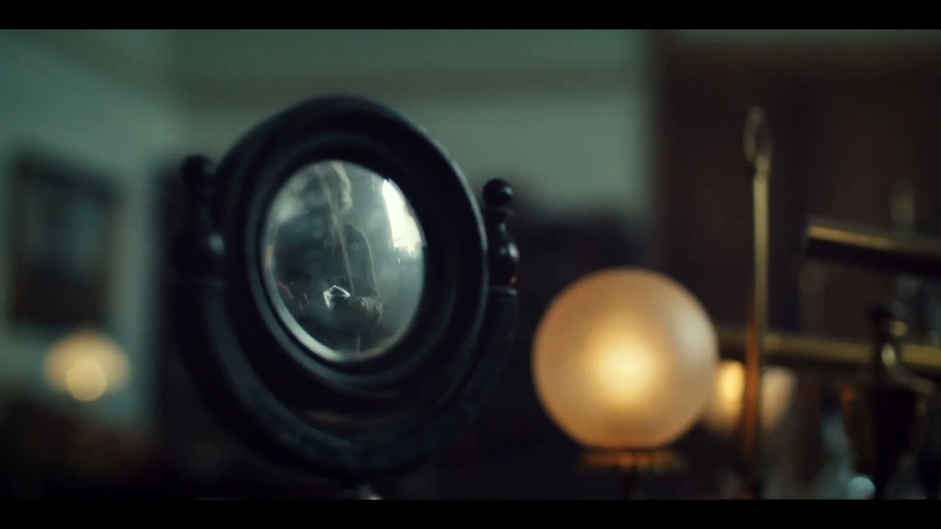 A vintage mirror reflects a person's silhouette as they move around a dimly lit room, with a glowing lamp in the foreground.