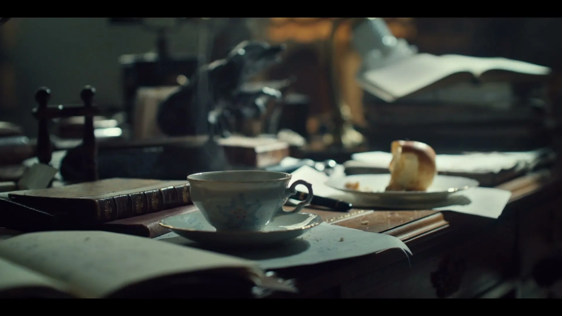 A steaming cup of tea sits on a cluttered wooden desk, surrounded by old books and papers, with a half-eaten apple on a plate in the background.