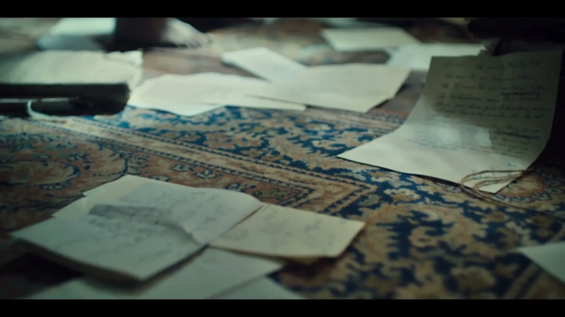 Bare feet walk across a patterned rug covered in scattered papers, some with scientific equations, in a dimly lit room.