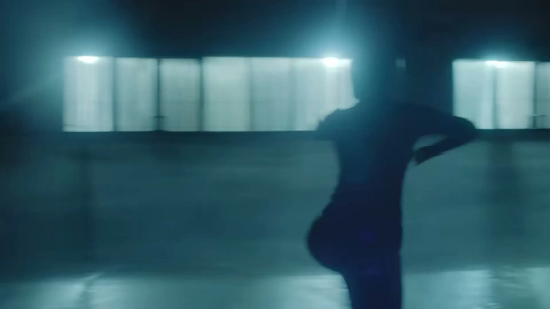 A female figure skater, silhouetted against bright lights, glides across an ice rink in a dark arena.