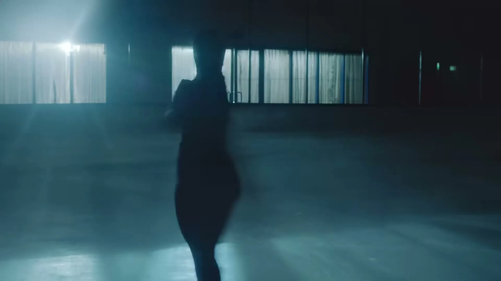 A female figure skater, silhouetted against bright lights, spins gracefully on an ice rink in a dark arena.