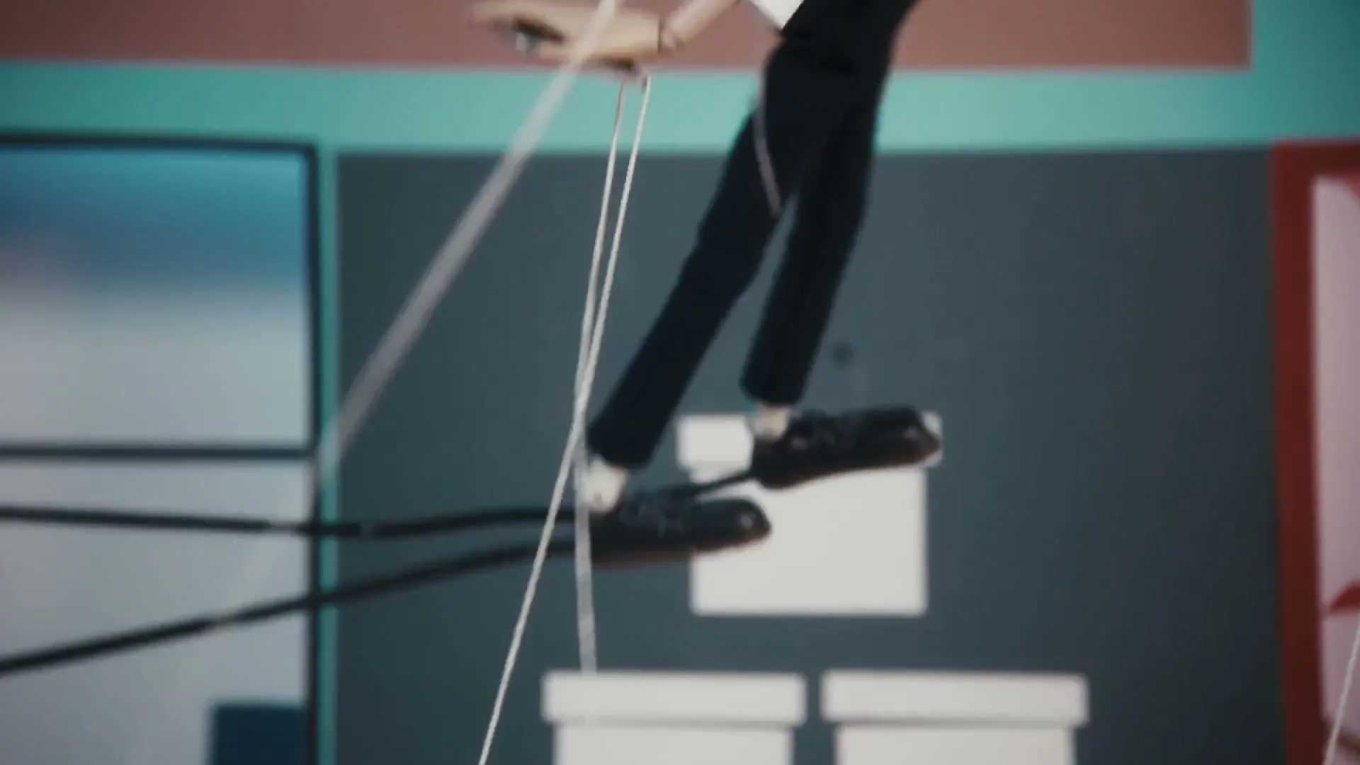 A male puppet with red hair and a mustache, wearing a white shirt and suspenders, is seen from the chest up, dancing with strings attached to him.