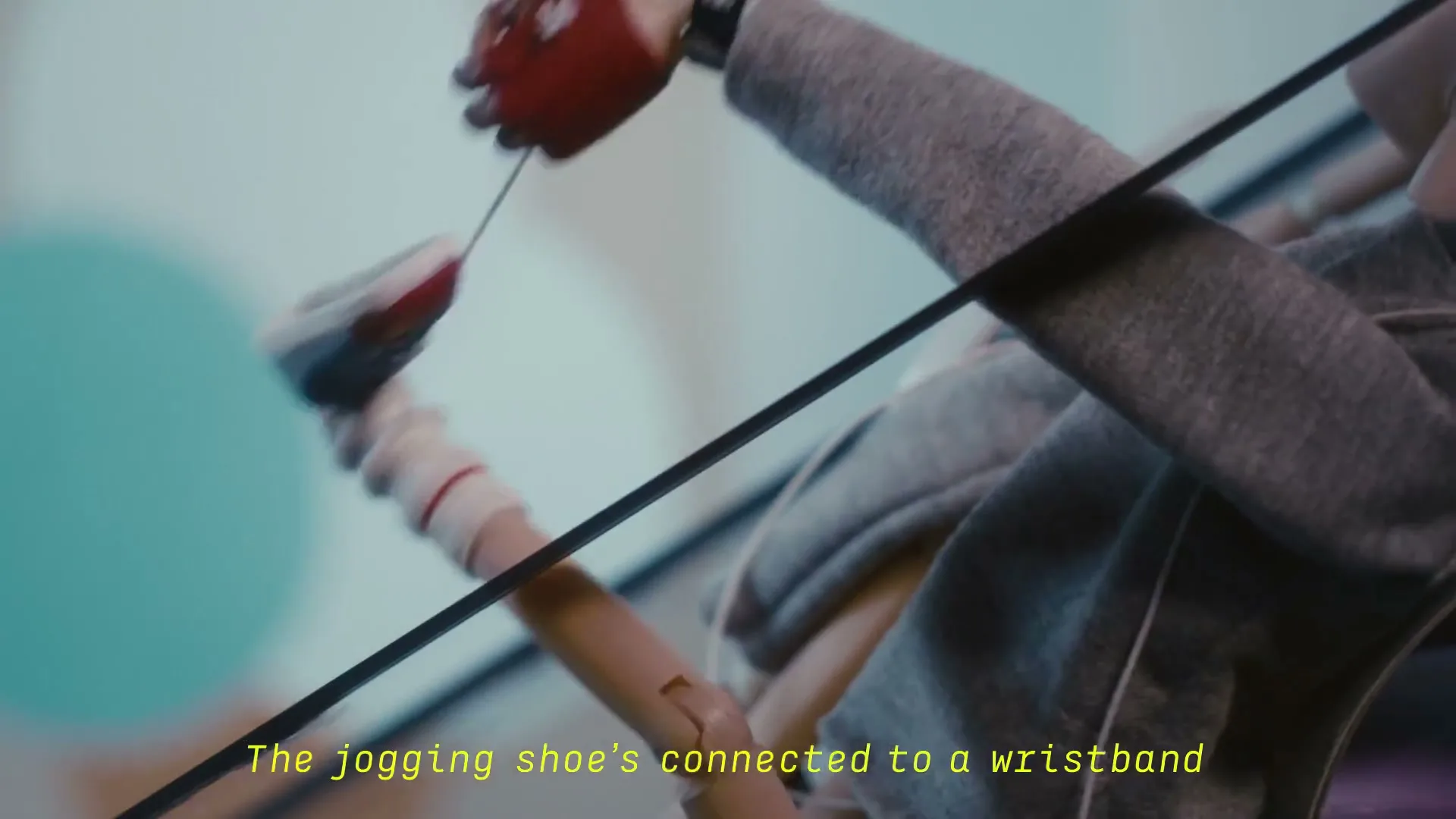 A puppet's arm and leg, dressed in a grey hoodie and a red glove, are connected by strings against a blurred, colorful background.