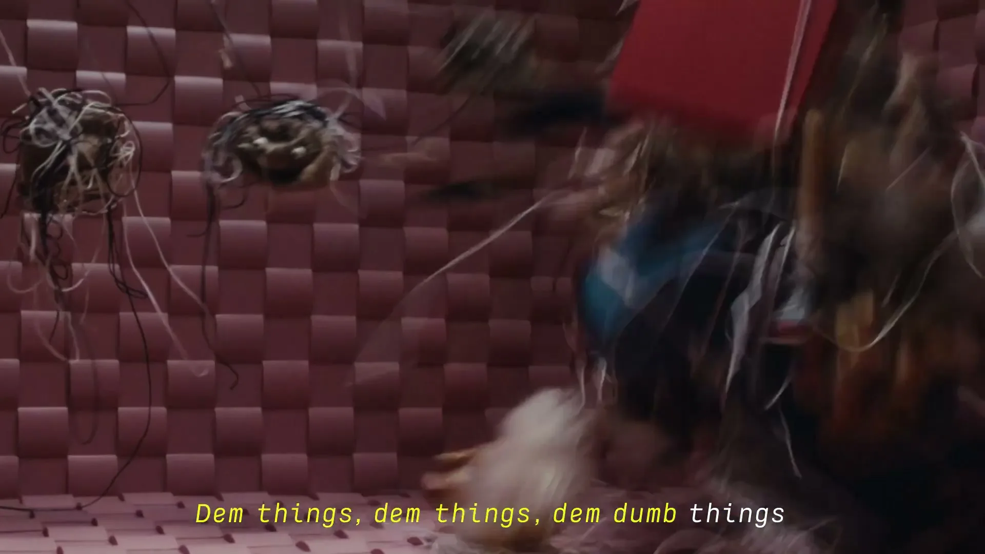 A chaotic jumble of wires and electronic waste tumbles rapidly through a pink, woven-textured room, with motion blur indicating fast movement.
