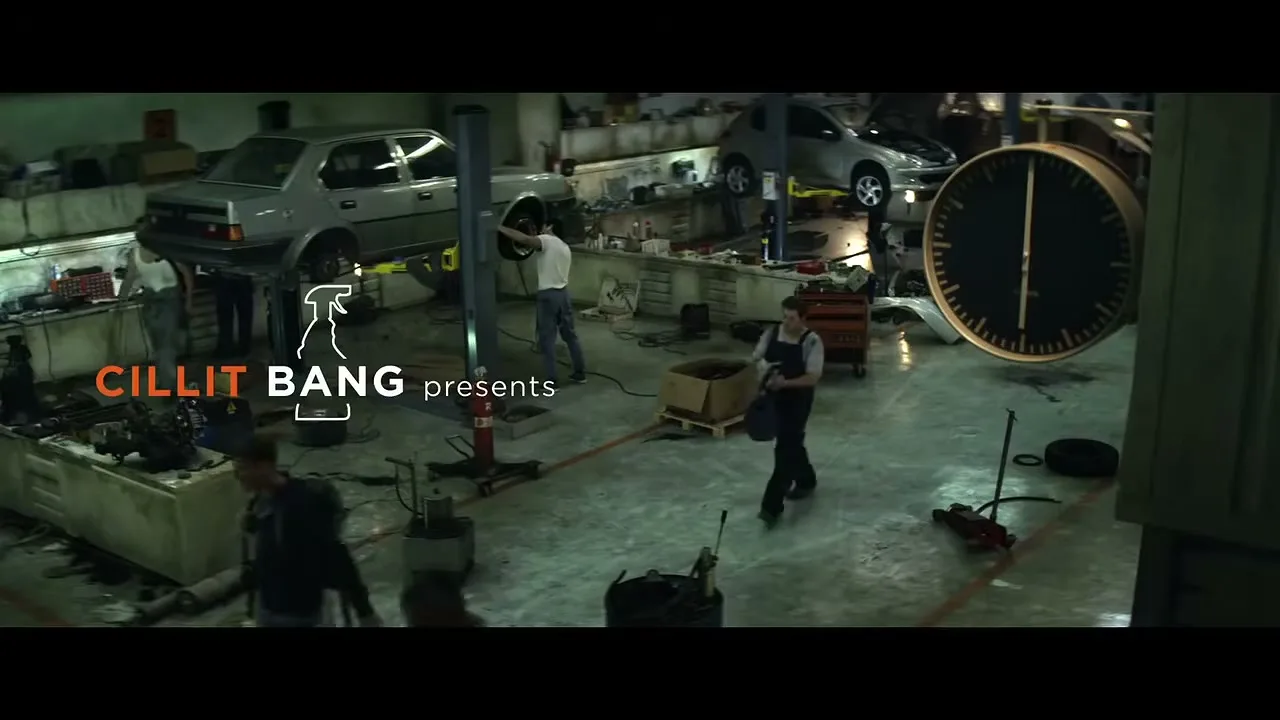 A wide shot of a busy, dimly lit car repair shop with several mechanics working on vehicles, and a large clock on the right.