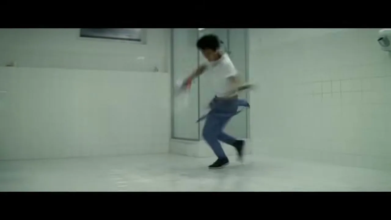 A man in a white t-shirt and blue pants dances energetically while cleaning a white tiled bathroom with a spray bottle and cloth.