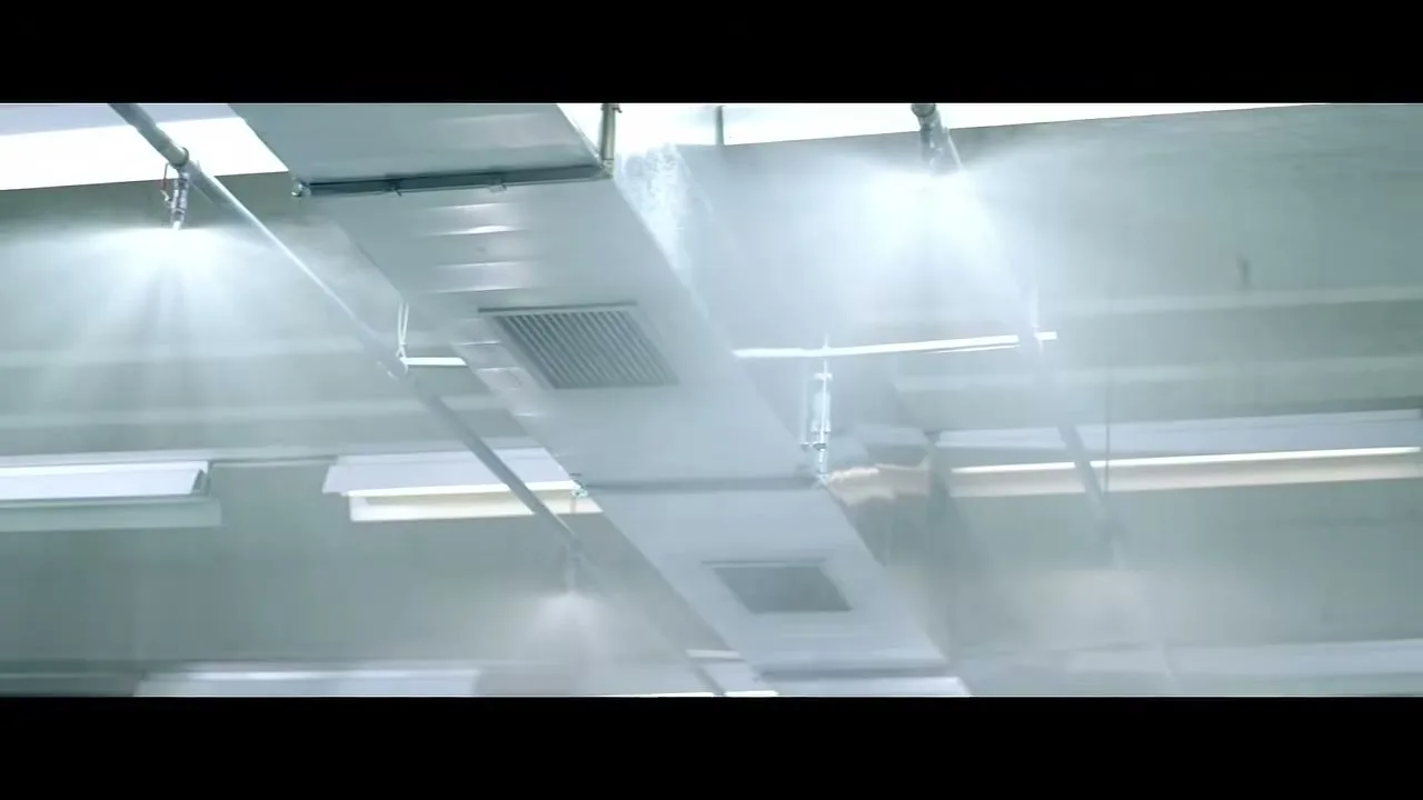 Water sprays from multiple sprinkler heads on the ceiling of a large industrial space, cleaning the air ducts.