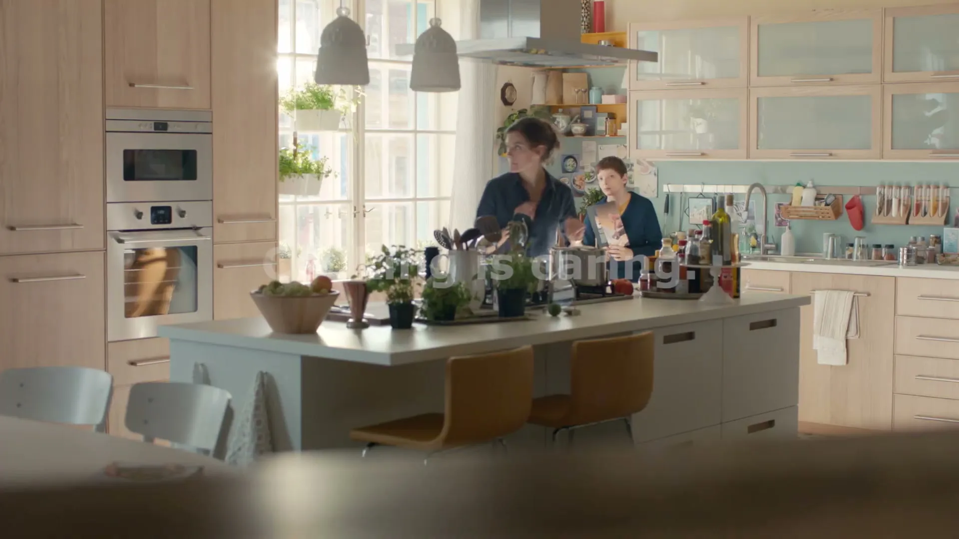 A woman and a child are cooking together in a bright, modern kitchen, with the text "Cooking is caring" overlaid.