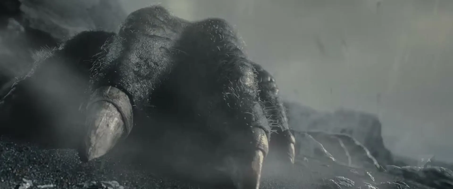 A giant, dark, clawed foot descends onto a rocky, misty landscape under a cloudy sky, kicking up dust and debris.