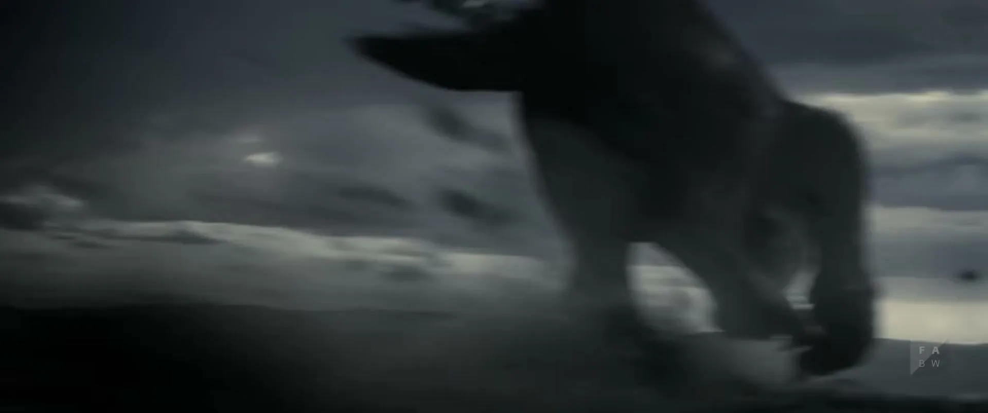 A large, dark, blurry creature with claws descends from the sky over a desolate, cloudy landscape, kicking up dust as it lands.