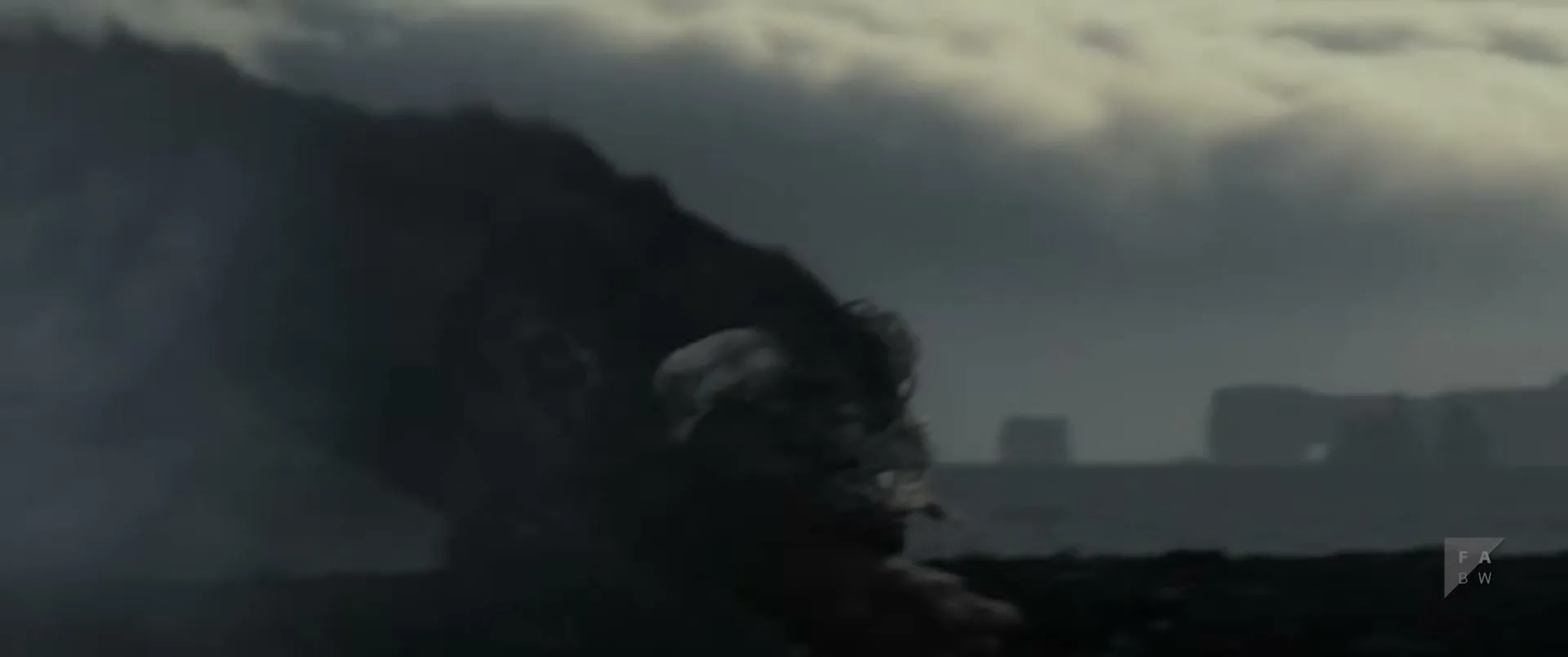 A dark, shadowy creature with a large head and body emerges from a dark, rocky landscape under a cloudy sky.