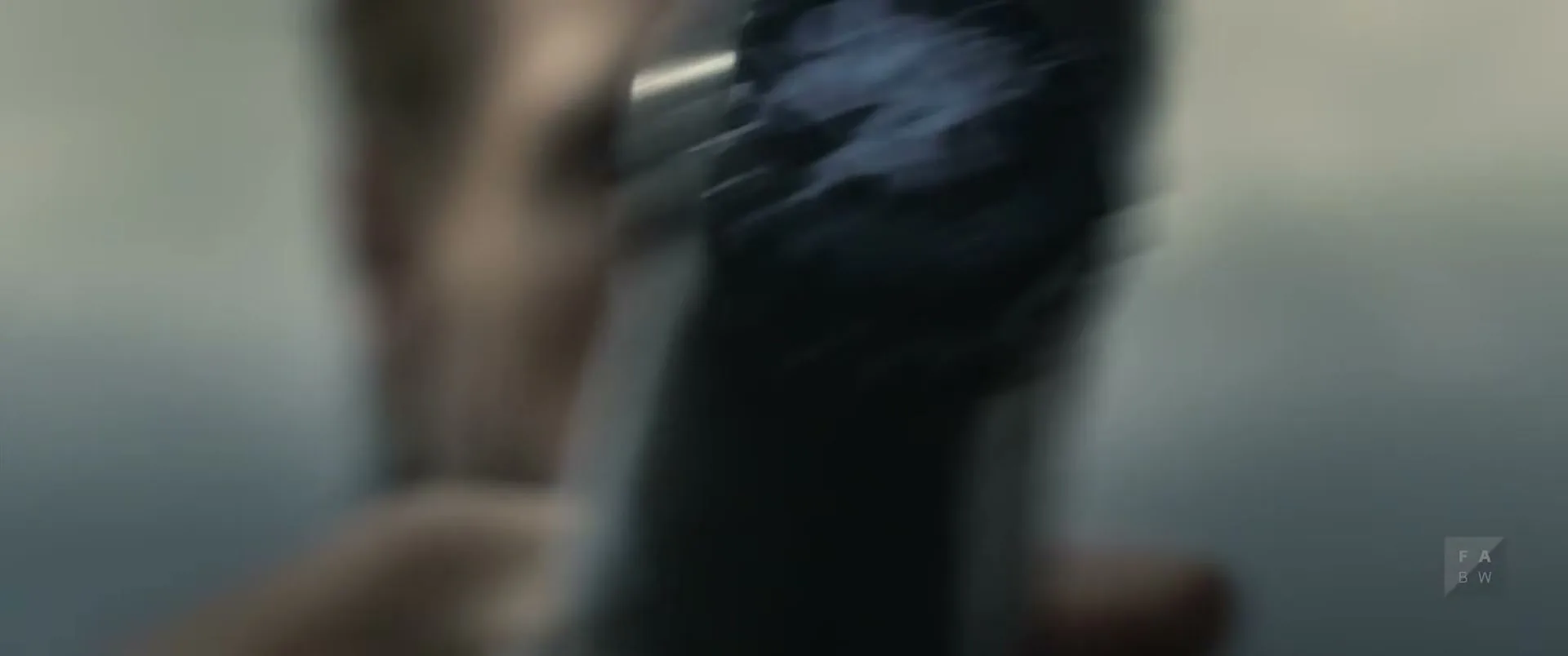 A man with a beard and dark clothing holds a beer bottle, which comes into focus to reveal the brand logo on the cap.