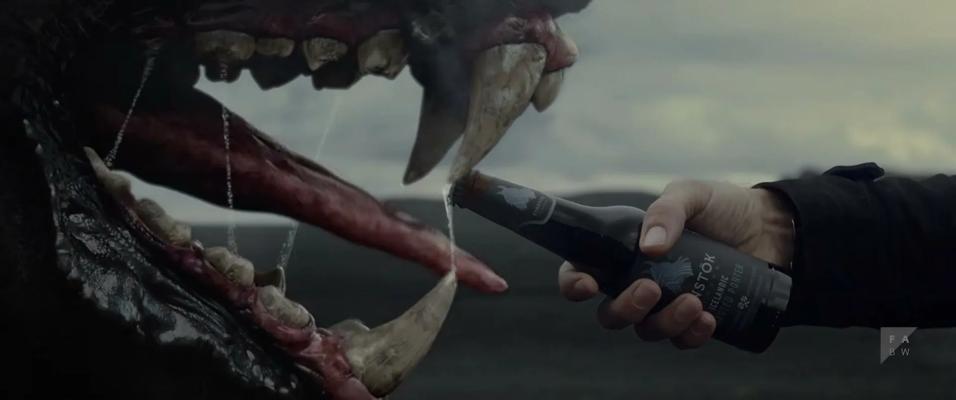 A person's hand opens a bottle of Einstök beer, with the cap flying off, next to a monster's open mouth with large fangs.