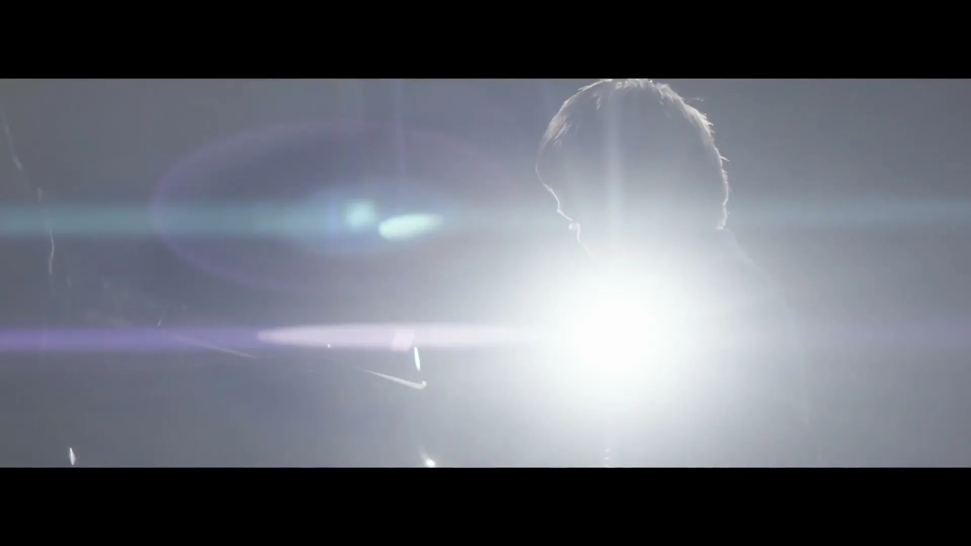 A young man is silhouetted by a bright light as he plays a grand piano on a stage, with a woman appearing in the background.