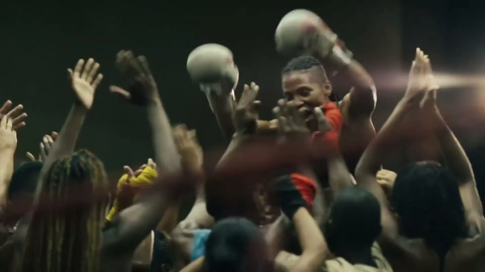 A female boxer with short hair and boxing gloves raises her arms in victory, surrounded by a cheering crowd in a boxing ring.