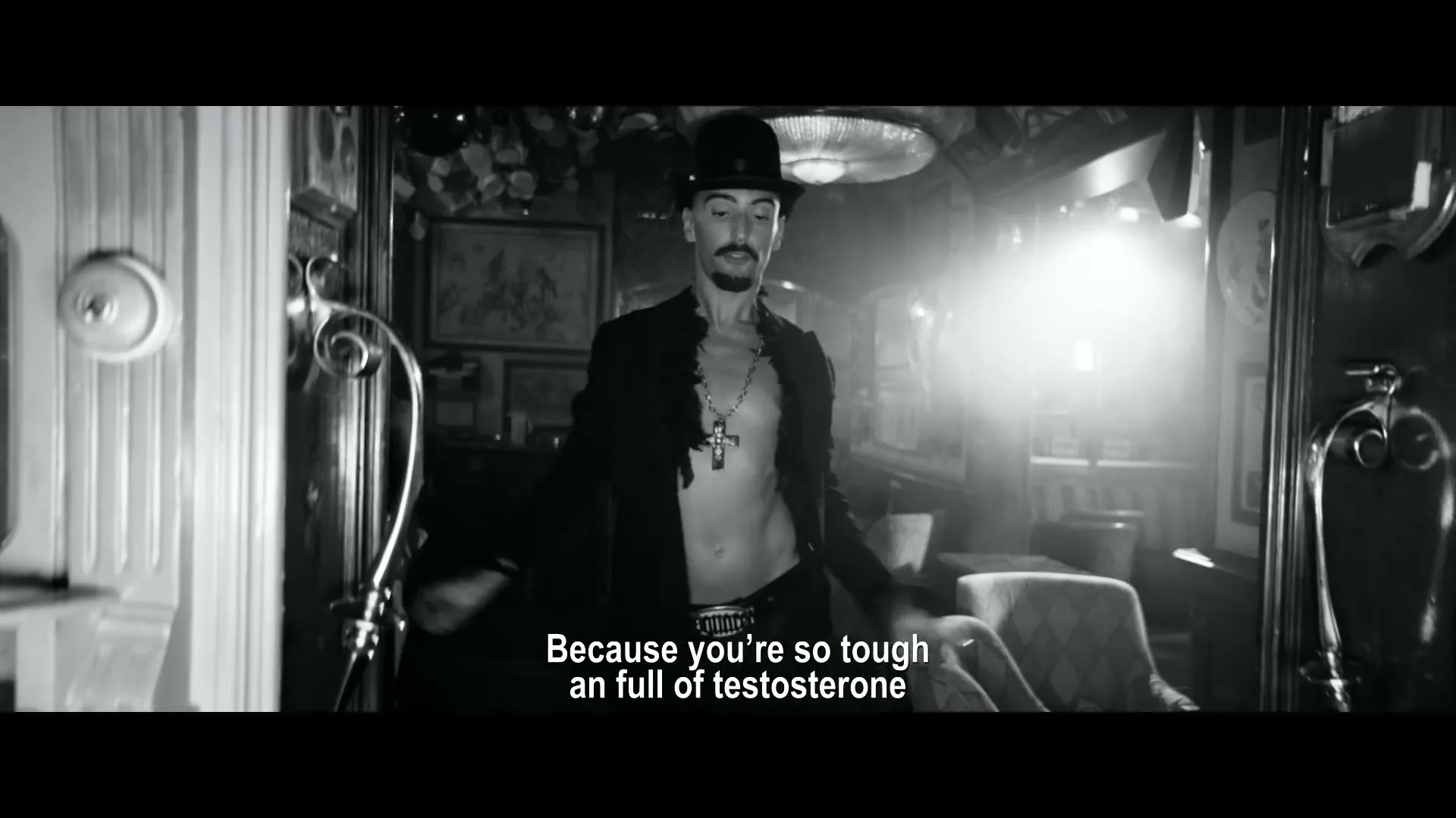 A man in a top hat and open shirt dances provocatively in a dimly lit, ornate bar, with other patrons visible in the background.