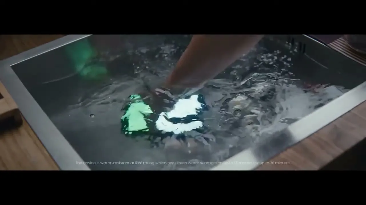 A hand reaches into a kitchen sink filled with water, splashing around a glowing smartphone to demonstrate its water resistance.
