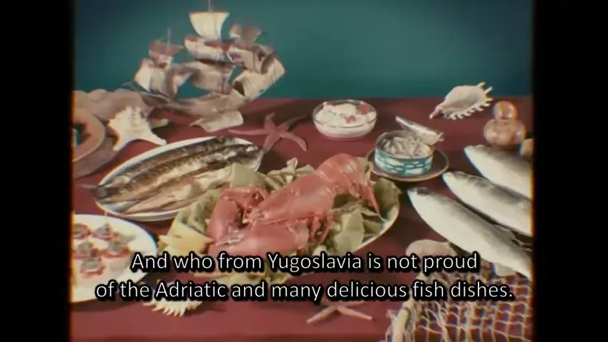 A table laden with various fish dishes, including a whole lobster, is shown in a retro-style setting, with a hand briefly entering the frame to gesture towards the food.
