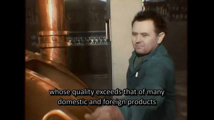 A man in a green jacket stands next to a large copper brewing vat, then a bottle of Zlaty Bazant 73 beer appears on a table.