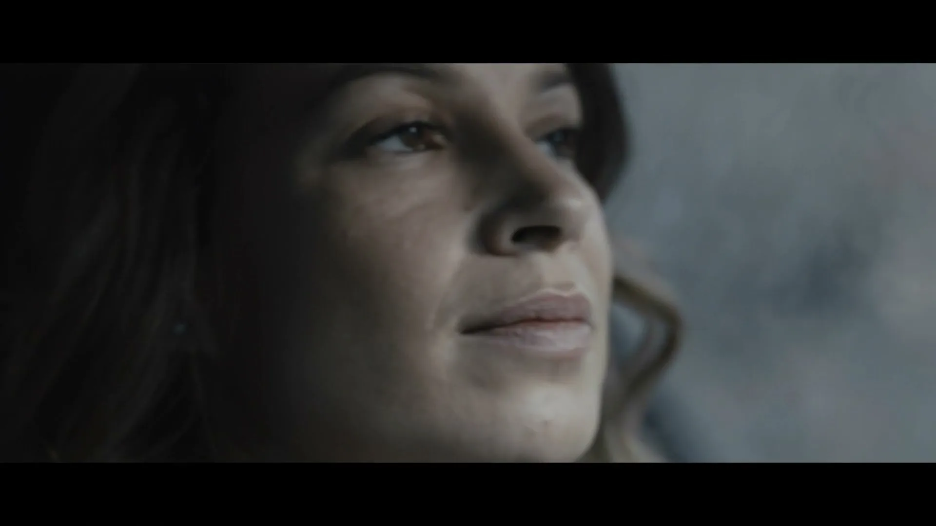 A woman with brown hair and a light complexion looks up and to the right, with a soft, contemplative expression, in a car interior.