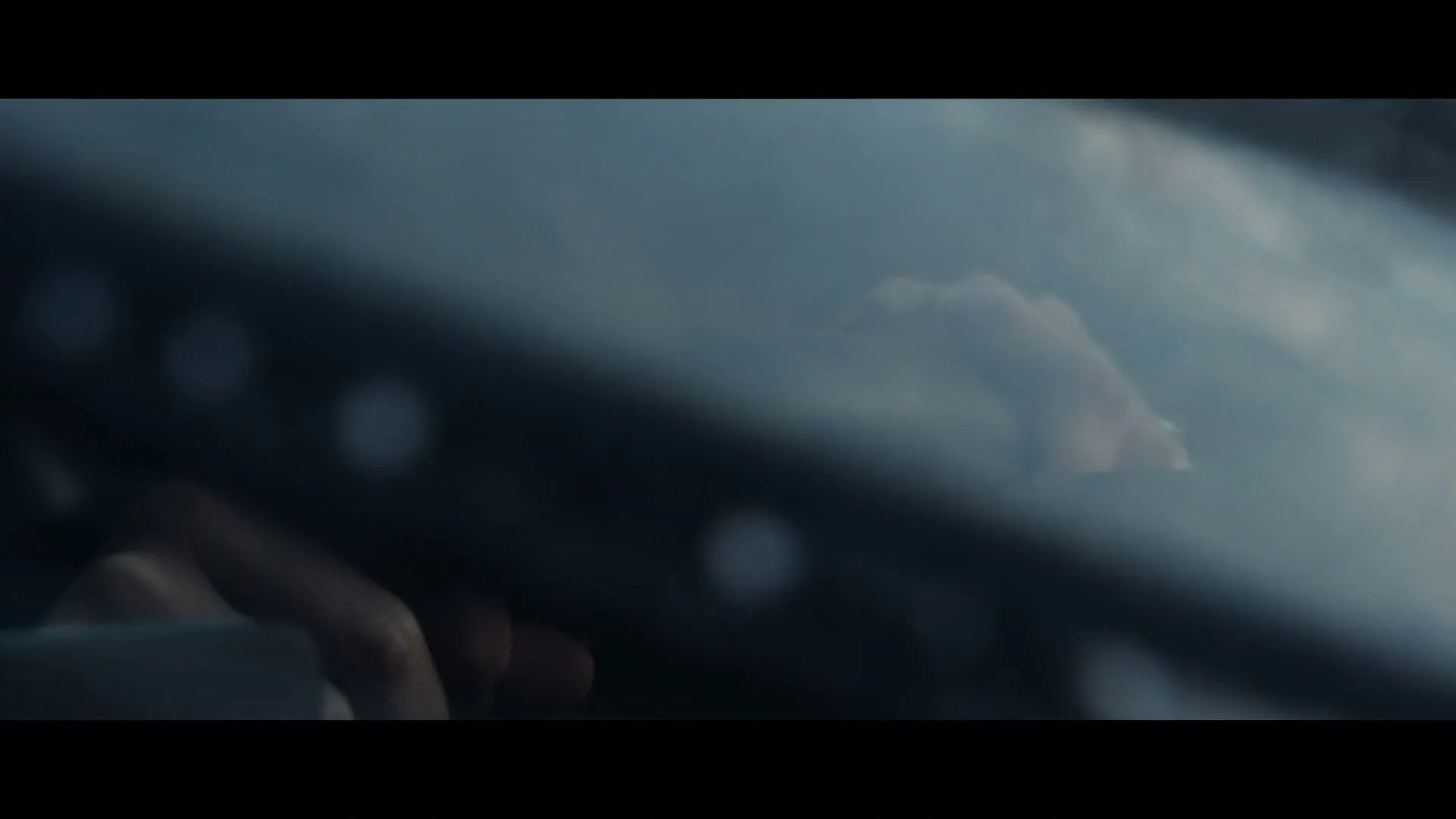 A blurry shot of a person's hands on a car dashboard, seen through a windshield, as the car moves.
