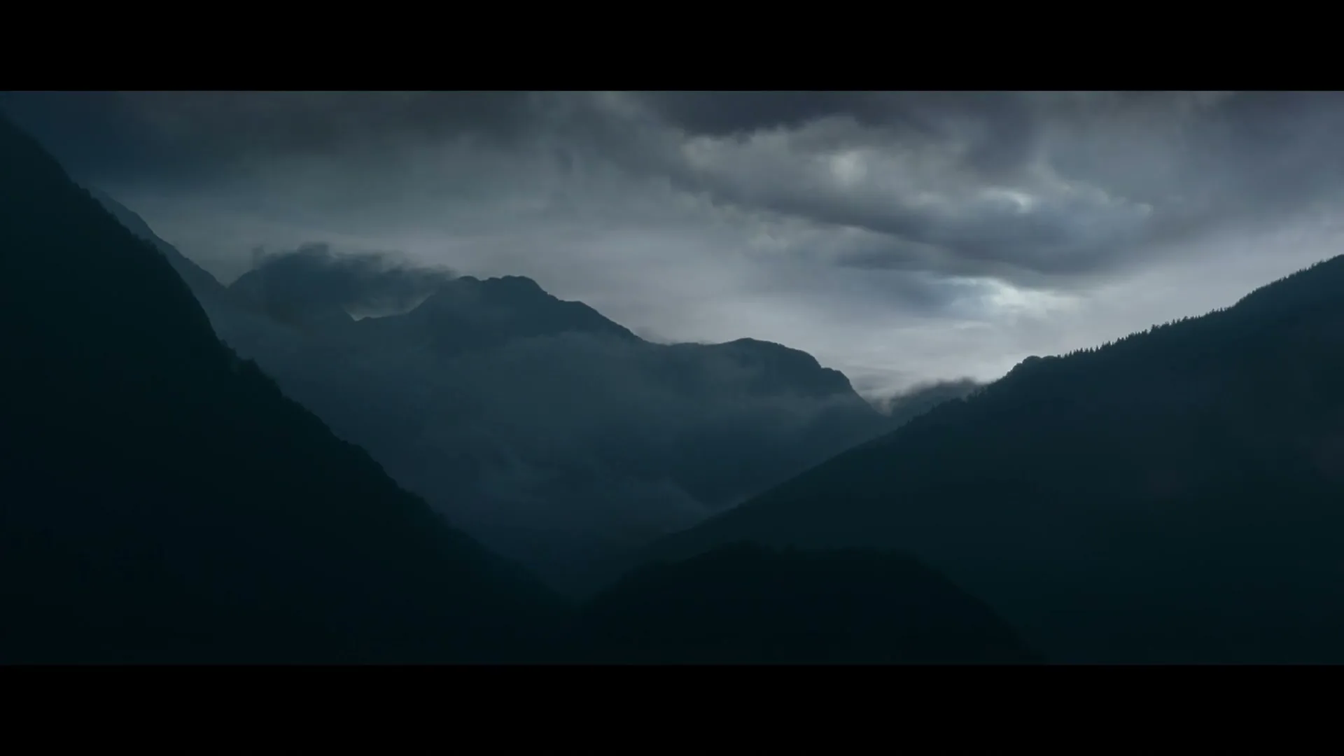 A wide shot of dark, misty mountains under a cloudy, ominous sky, with no people or products visible.
