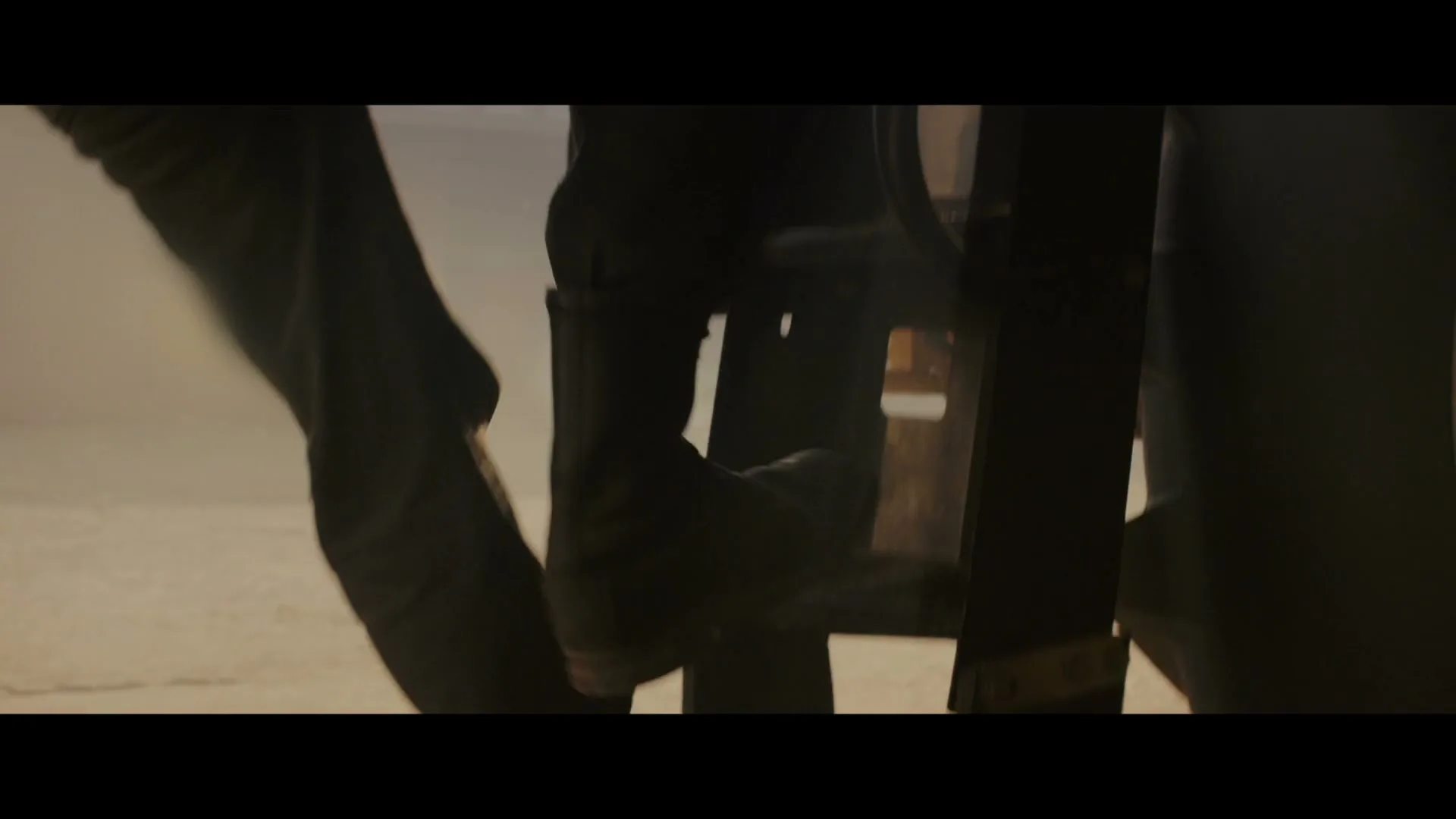 A person's legs in dark pants and boots are seen climbing a ladder in a dusty, hazy environment, with light visible in the background.
