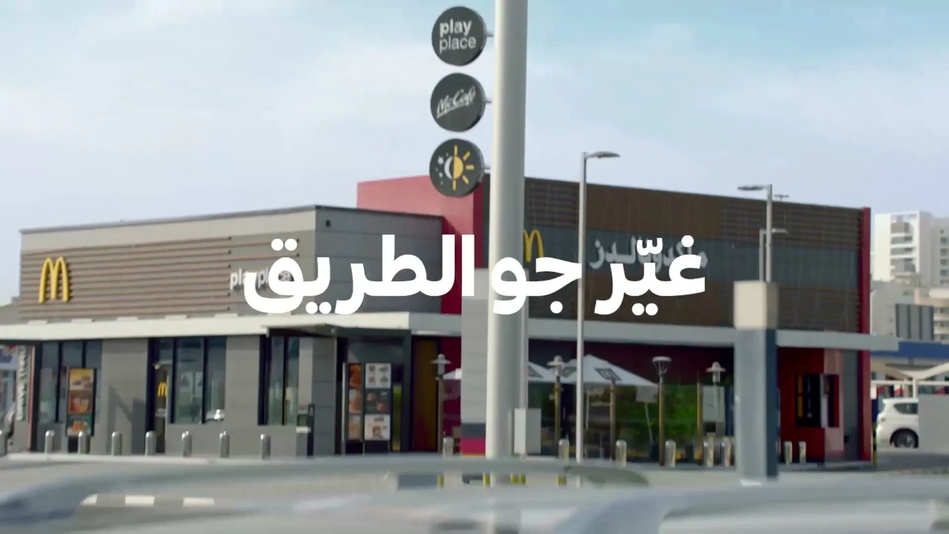 A family in a car drives up to a McDonald's drive-thru, with the golden arches sign visible against a blue sky.