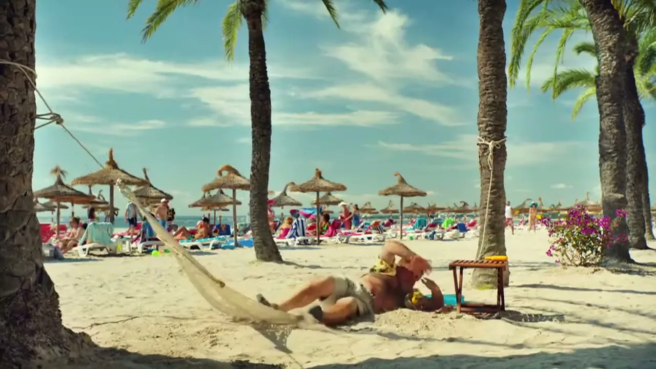 A man in a Hawaiian shirt and shorts falls out of a hammock on a sunny beach, surrounded by palm trees and other beachgoers.