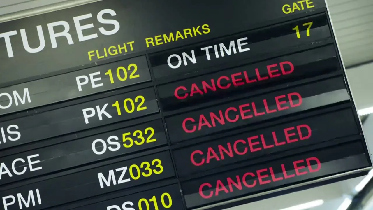 A close-up shot of an airport departures board, showing multiple flights changing from "ON TIME" to "CANCELLED" in red text.