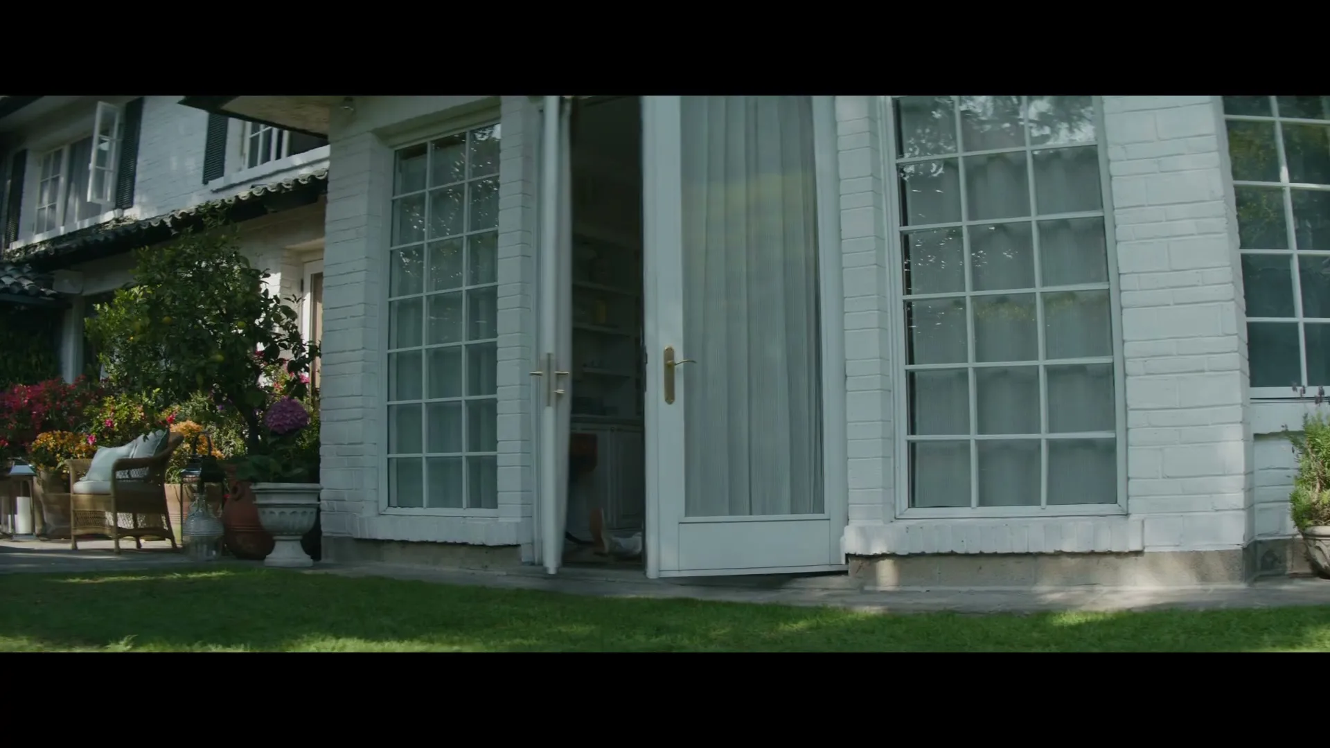 A person in a grey rabbit costume drags a man out of a white house and onto the green lawn in broad daylight.